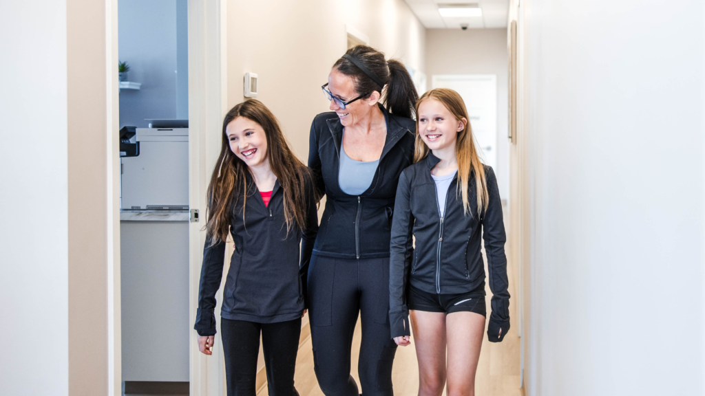 Mom walking with her two daughters through Transcend Headache Clinic after fall sports practice.